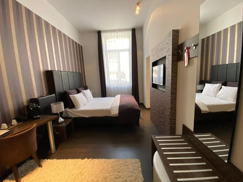Hotel bedroom with striped wallpaper, dark wood floors, and a large mirror reflecting the bed.