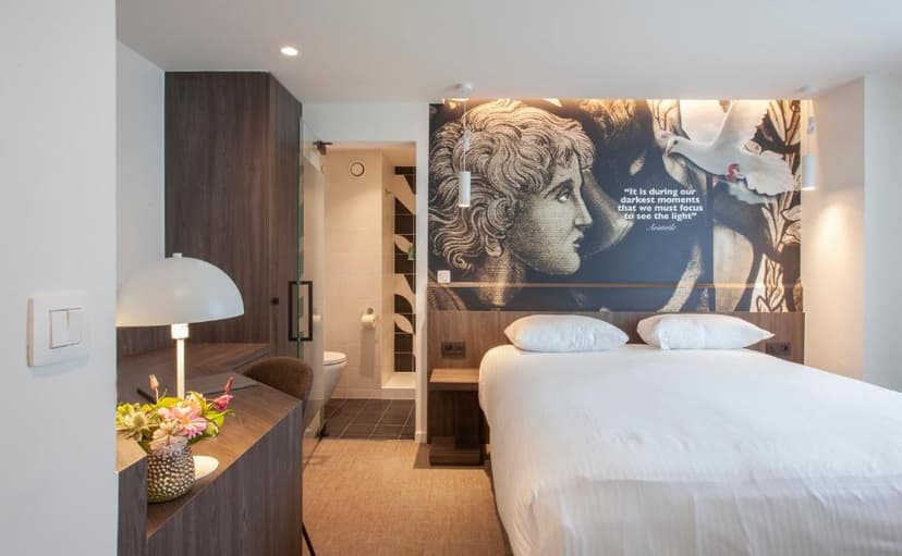 Hotel room with white bedding, desk, and wall art featuring a classical profile and a dove.