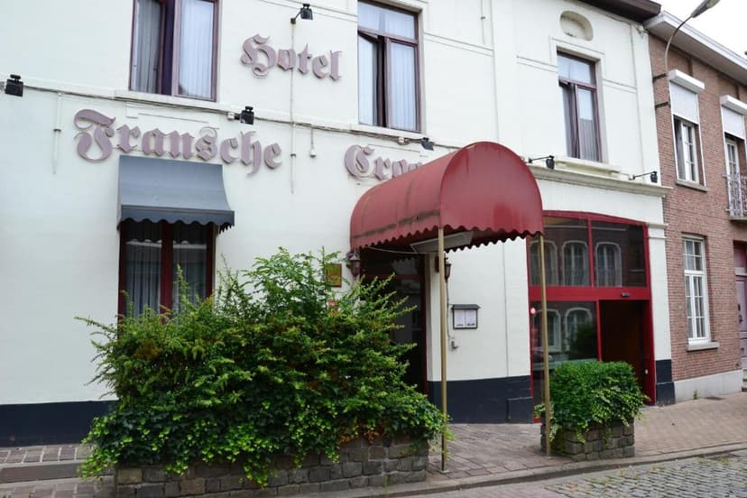 Hotel Fransche Crn facade with red awning and green bushes on cobblestone street