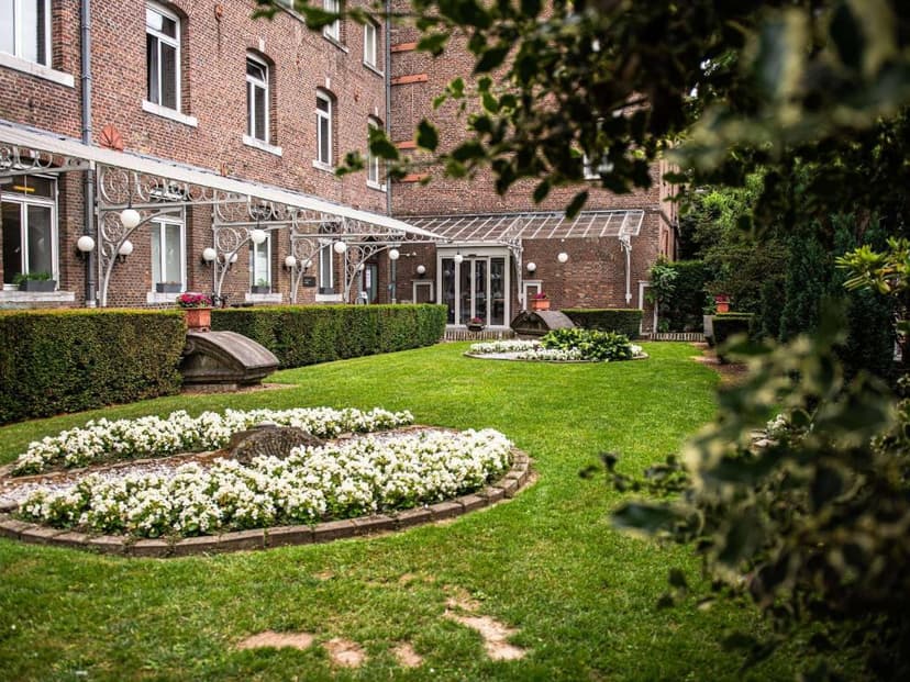 Manicured garden with white flowers and hedge in front of a brick building with glass awning.