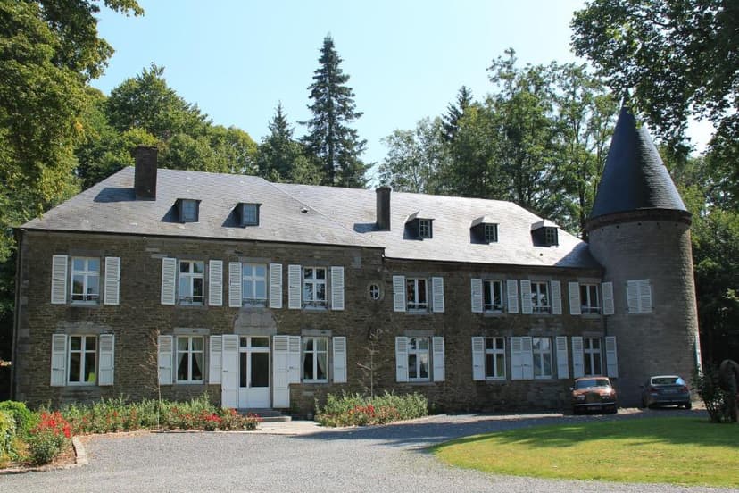 Stone chateau with white shutters and conical tower surrounded by green trees