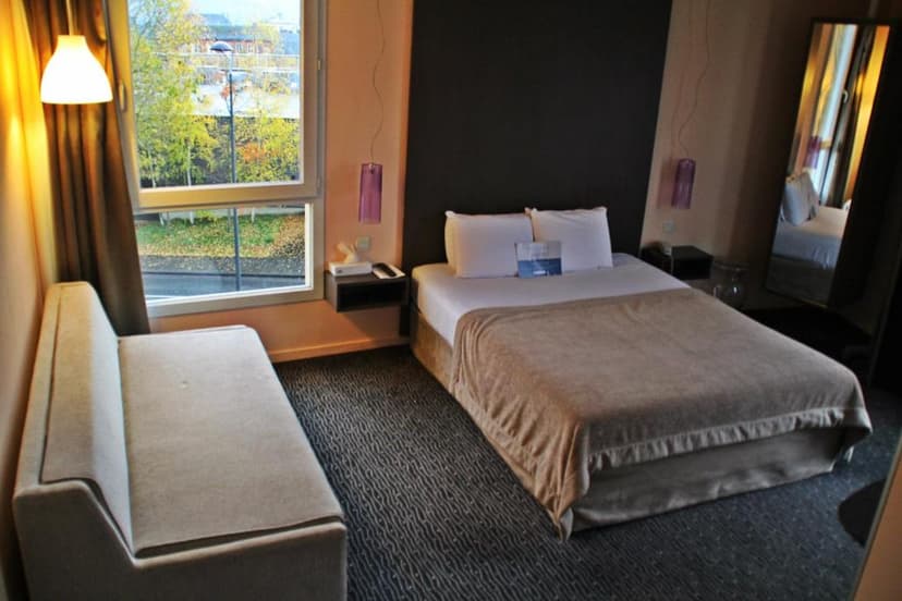 Hotel room with double bed, light sofa, and window view of autumn trees.