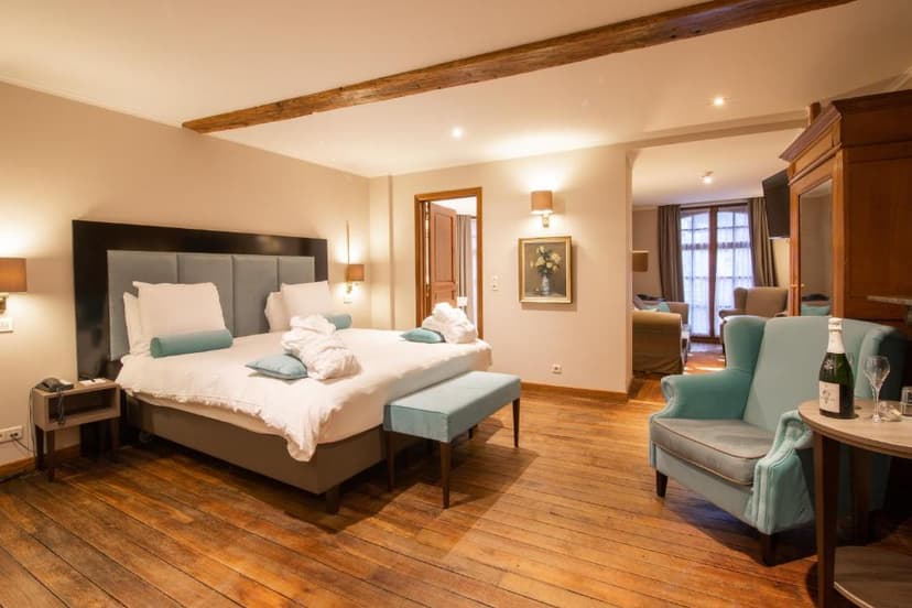 Hotel bedroom with large bed, wood floors, and plush seating area with champagne.