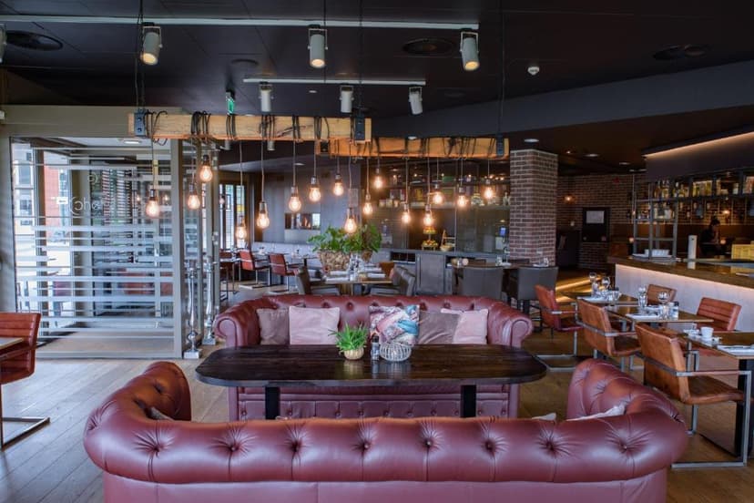 Restaurant interior with leather Chesterfield sofas, wooden tables, and exposed bulb lighting.