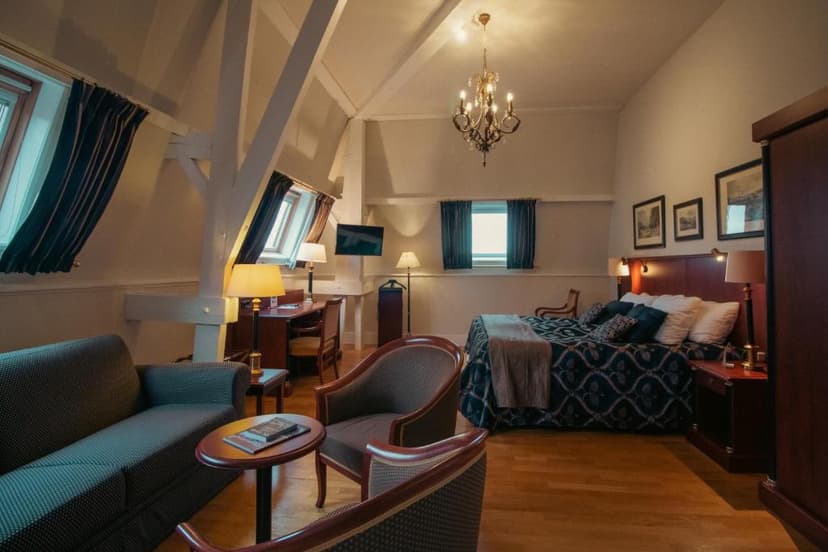 Attic hotel suite with exposed beams, chandelier, sitting area, and large bed