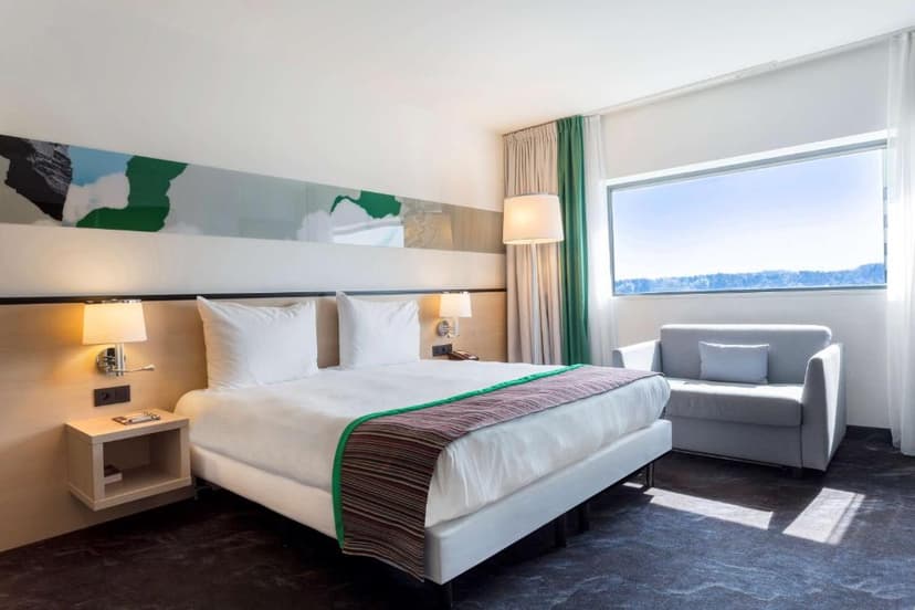 Modern hotel bedroom with white bedding, modern art, and a large window view of snowy landscape.