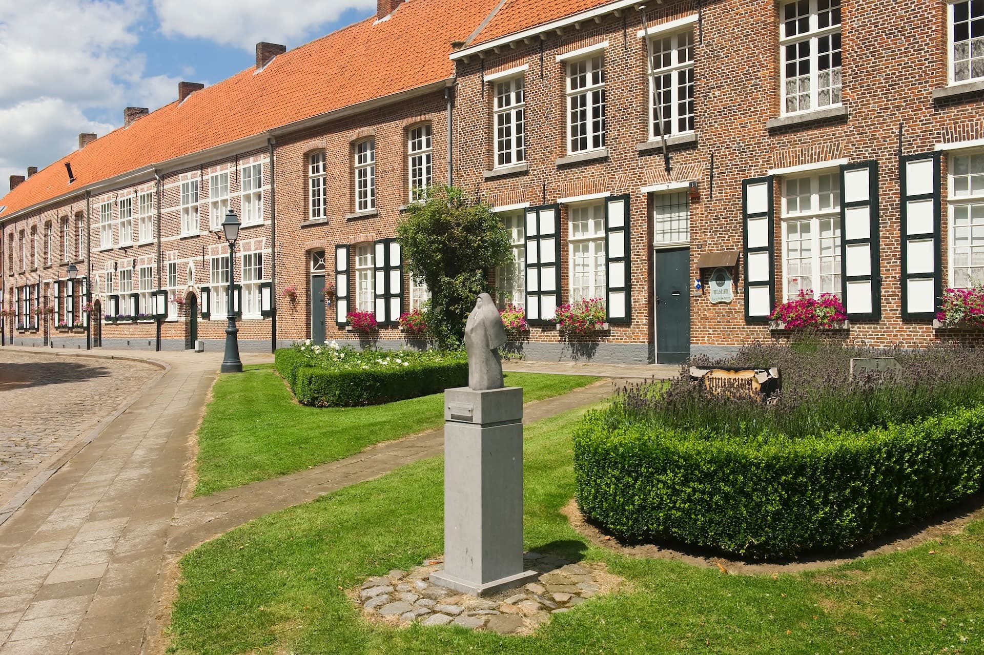 Brick almshouses with orange tile roofs, green lawns, and a statue in Turnhout.