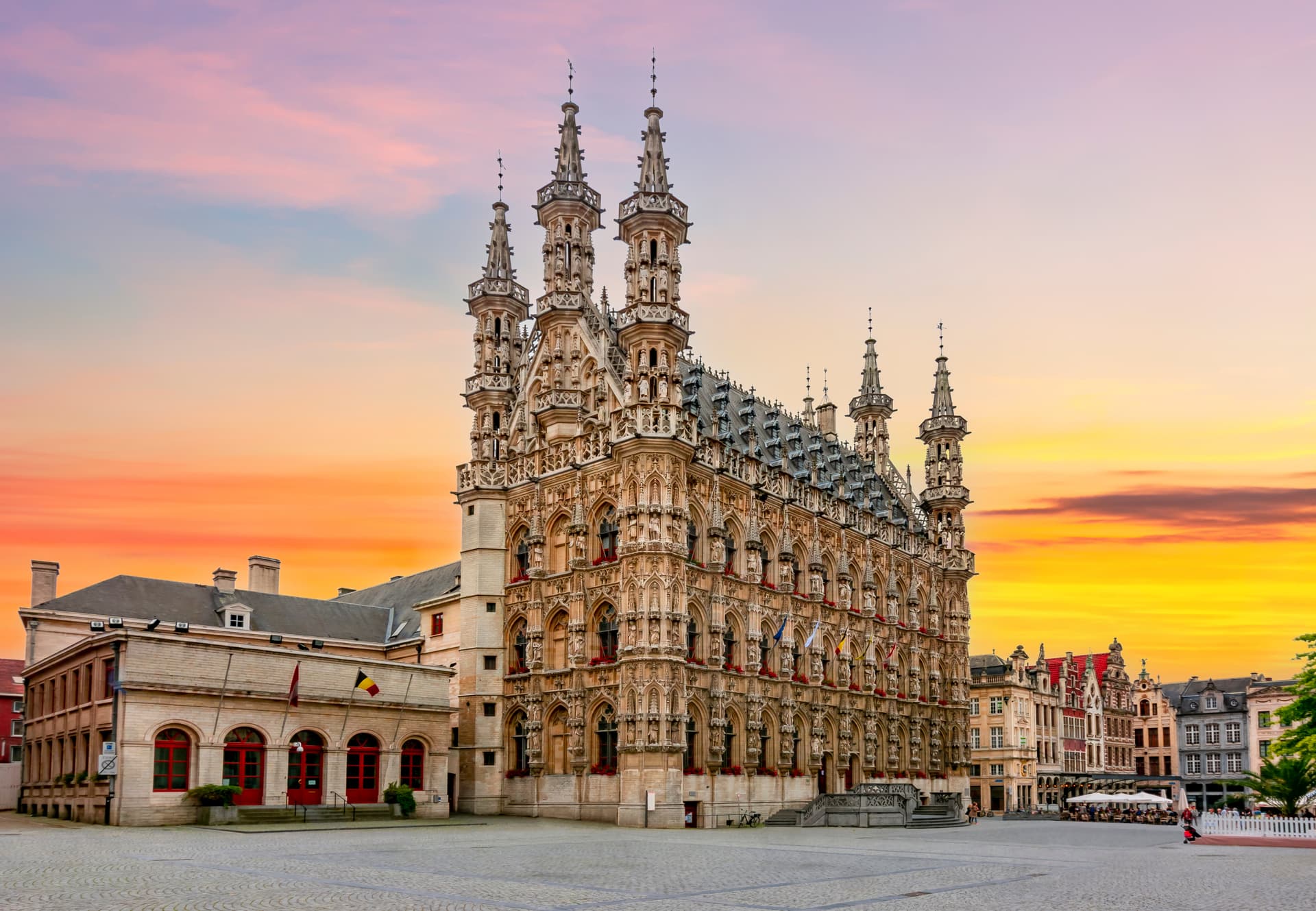 Ornate Gothic Town Hall in Leuven, Belgium, against a vibrant orange and pink sunset sky.