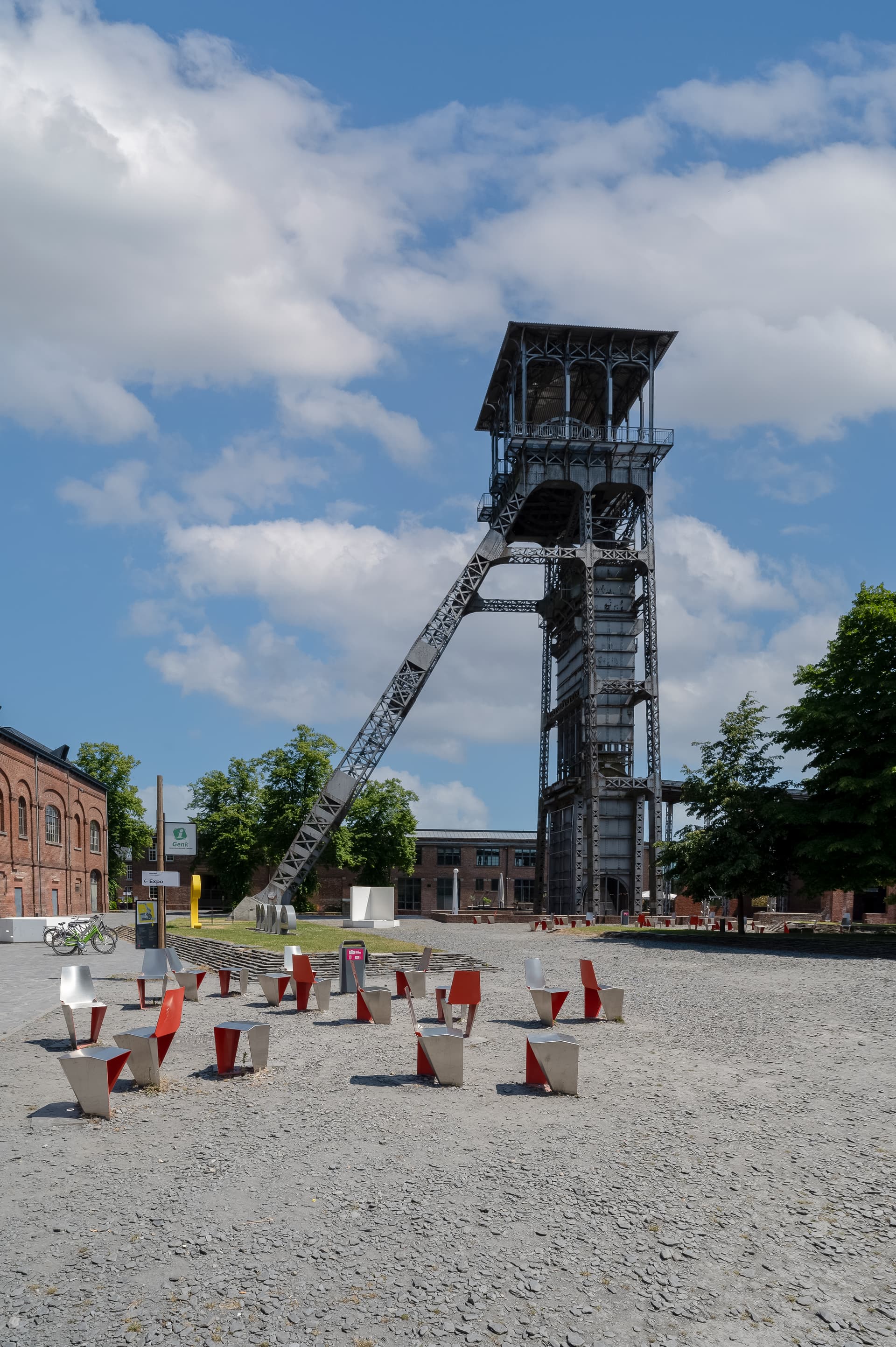 Industrial headframe structure with modern seating area and brick buildings under a blue sky.