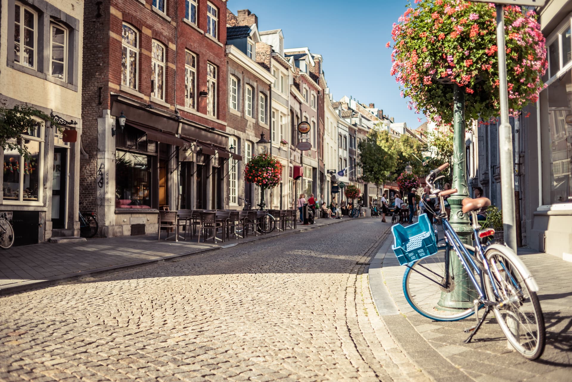 Bicycle parked on cobblestone street lined with shops and outdoor cafe seating in Maastricht.