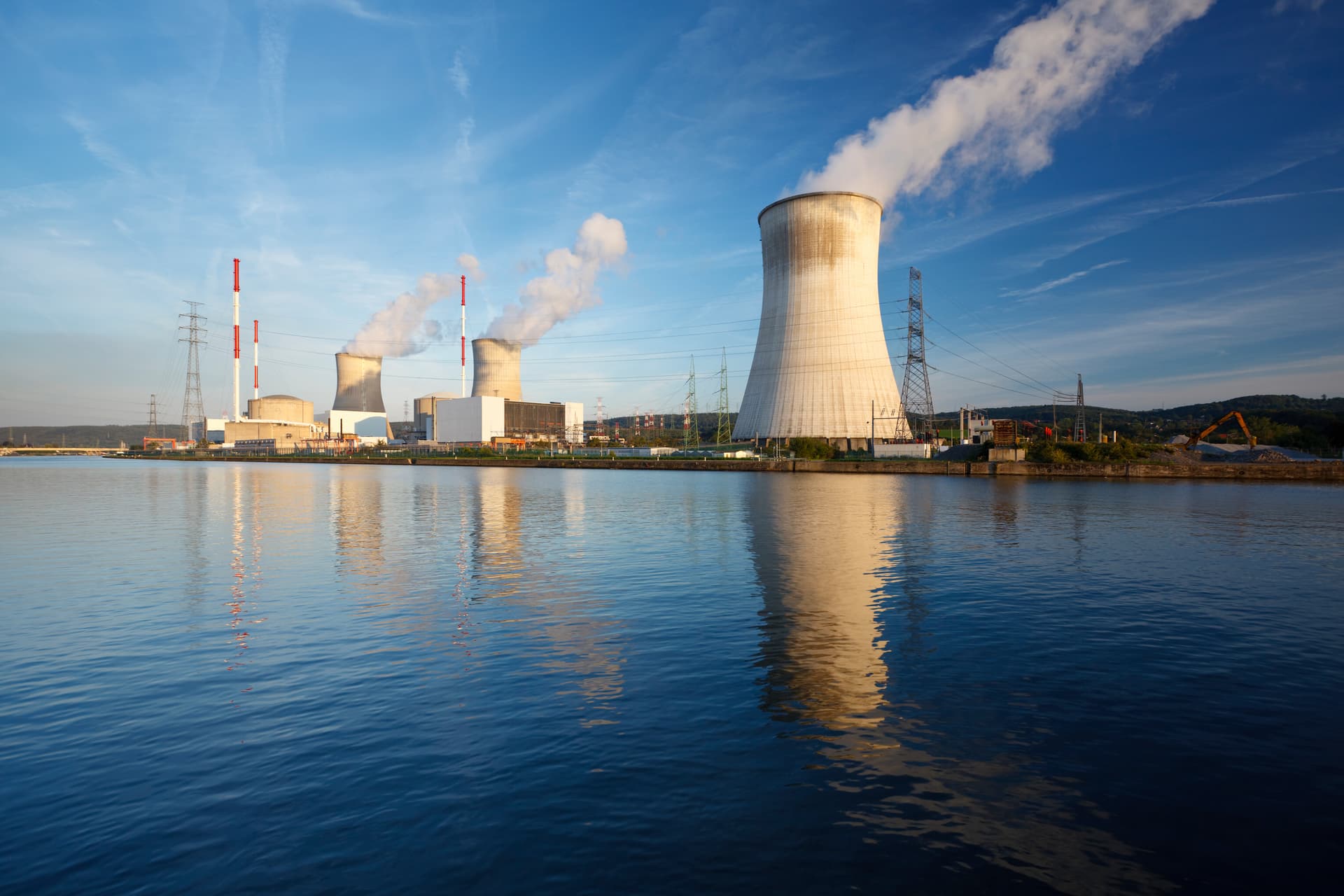Nuclear power plant cooling towers emitting steam over calm blue water, Tihange.