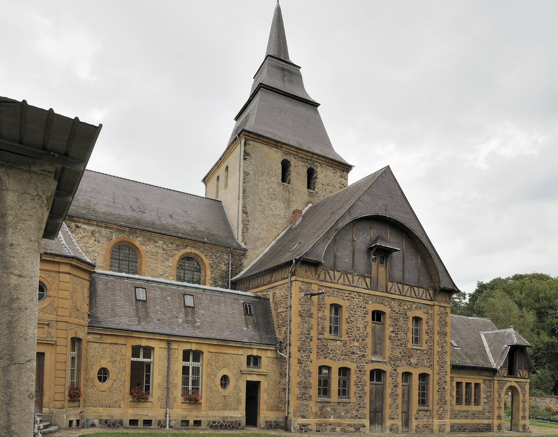 Stone church building with slate spire and yellow trim under an overcast sky, Laval, France.