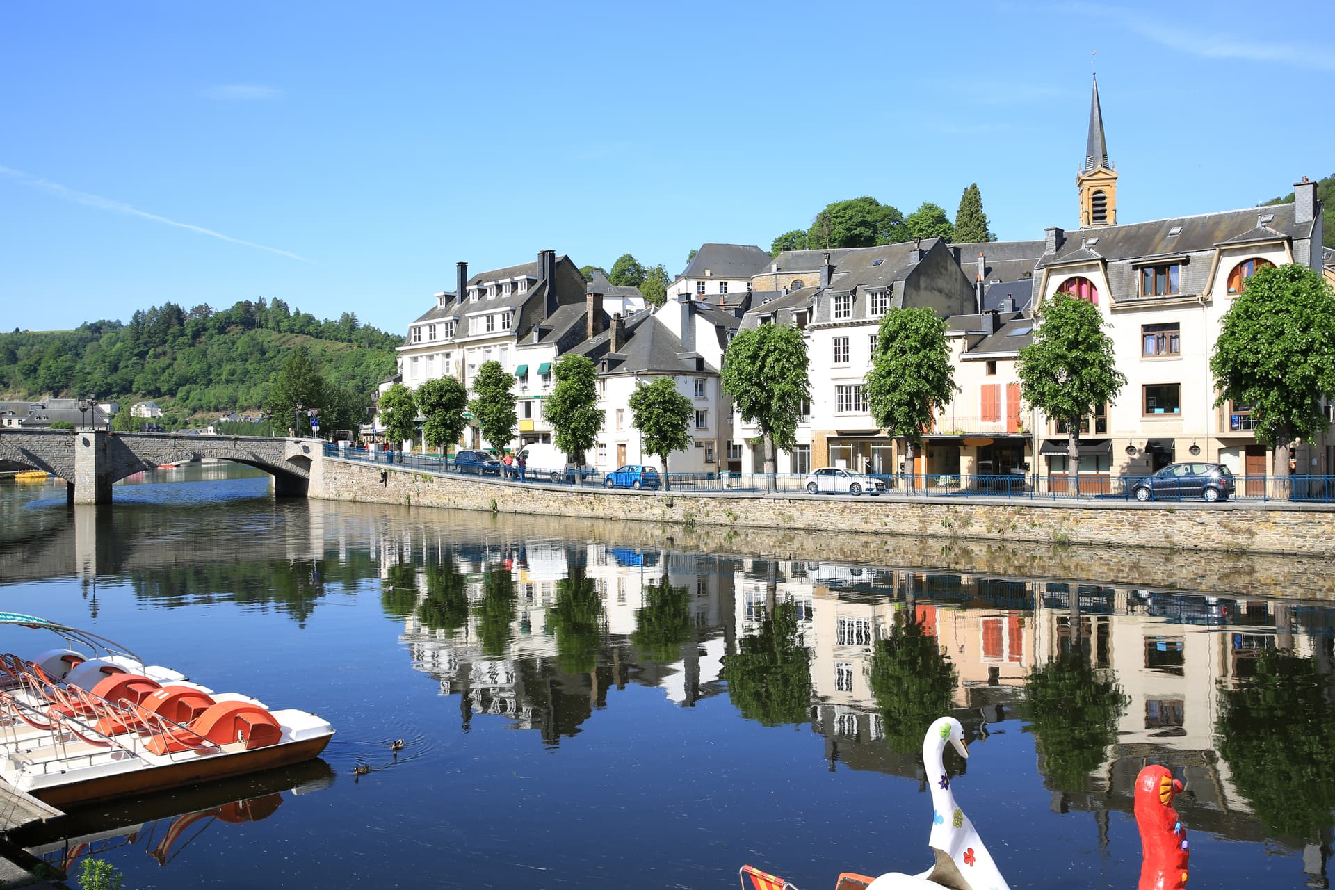 Pedal boats docked on river next to town with stone bridge and church spire