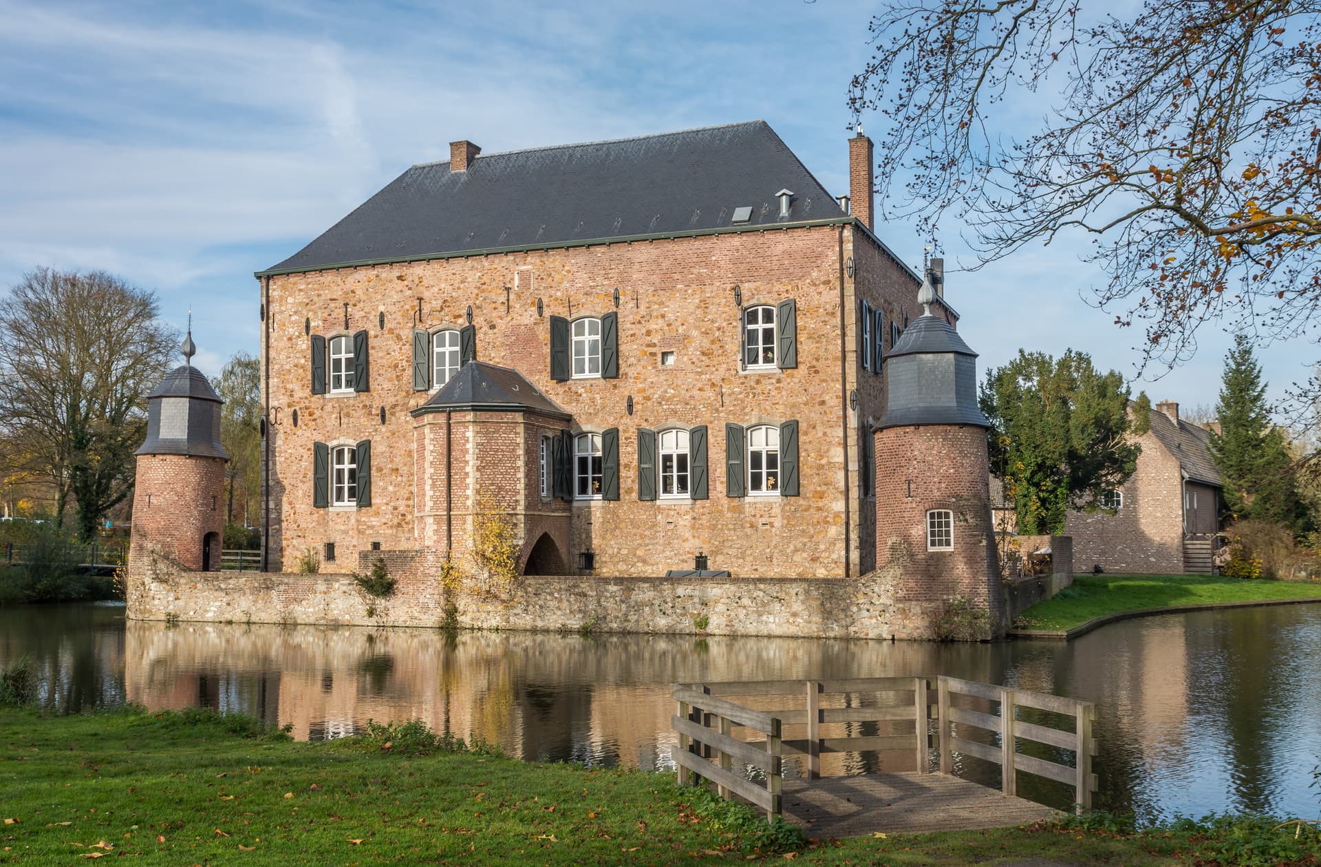 Stone castle with turrets surrounded by a moat, reflected in the water under a blue sky.