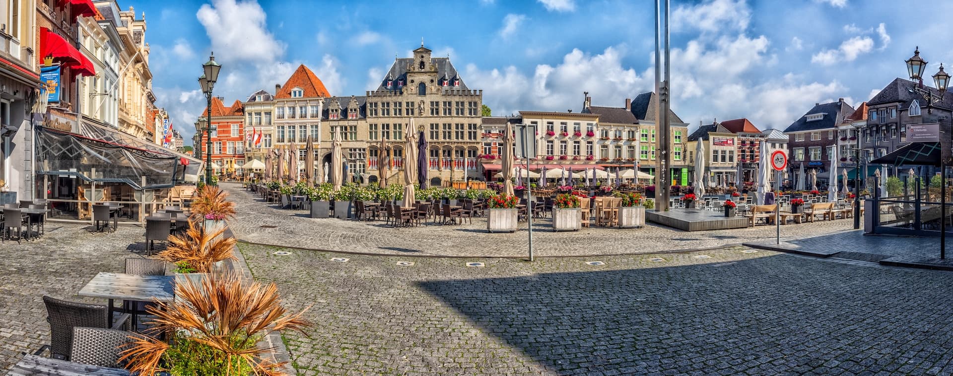 Cobblestone town square with outdoor cafe seating and historic European buildings under blue sky.