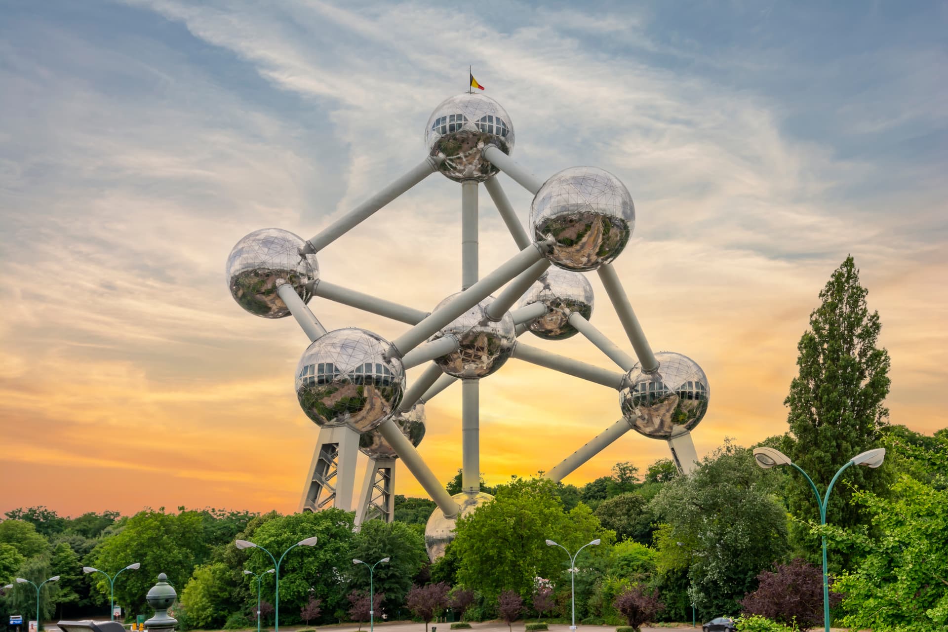 Atomium structure in Brussels against a sunset sky above green trees and park area.