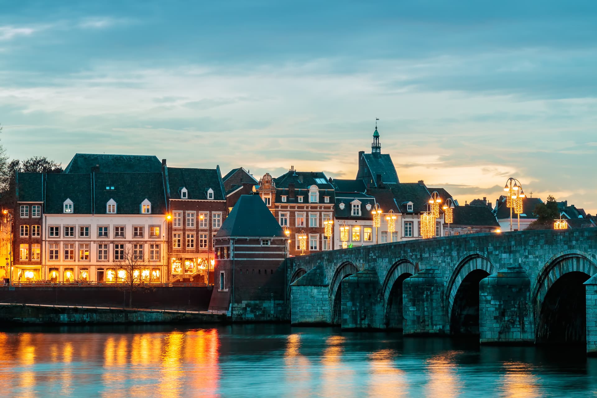 Stone arch bridge over water reflecting illuminated historic buildings at dusk.
