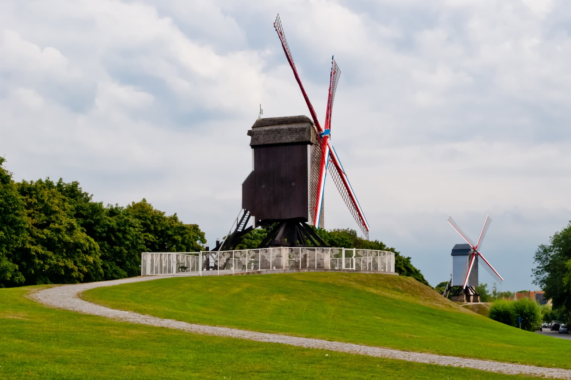 Wooden windmill with red and white sails on a grassy hill under cloudy sky