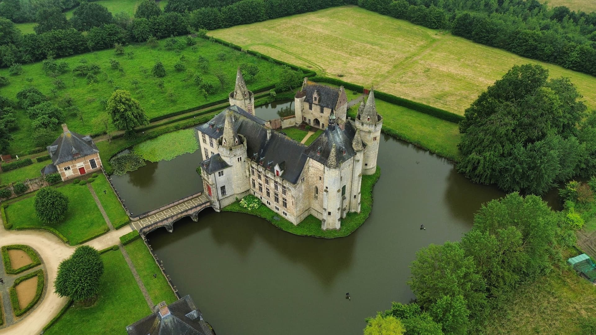 Aerial view of a historic moated castle surrounded by lush green fields and dense forest.