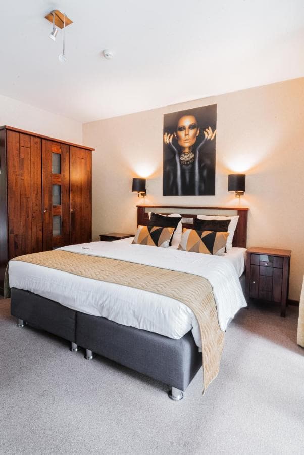 Hotel bedroom with large bed, wooden wardrobe, and modern portrait art above headboard