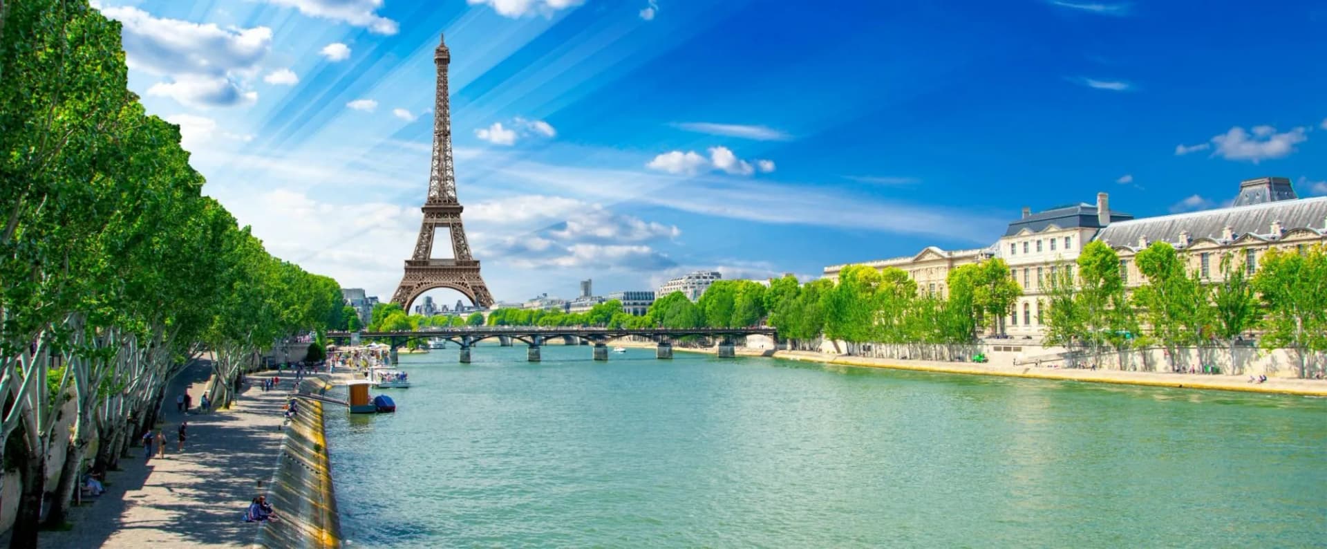 Eiffel Tower over the Seine River with tree-lined banks and historic buildings in Paris.