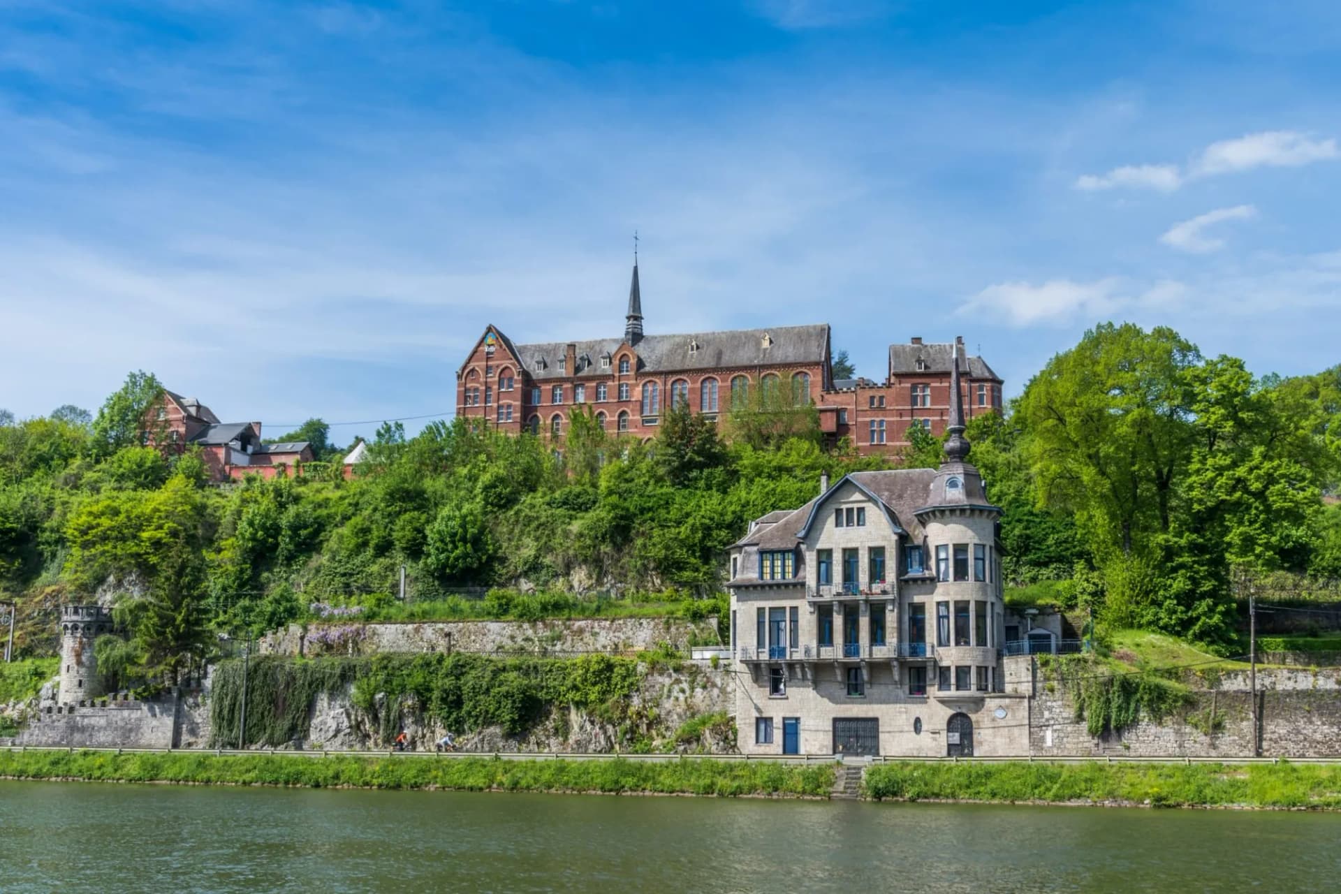 Buildings on a steep, green hillside above a river in Dinant, Belgium.