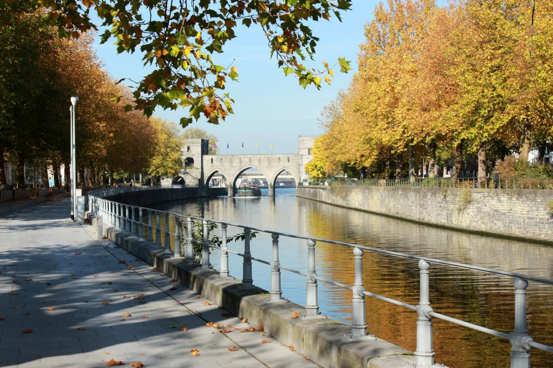 Canal with arched stone bridge, autumn trees, and paved walkway in Doornik.