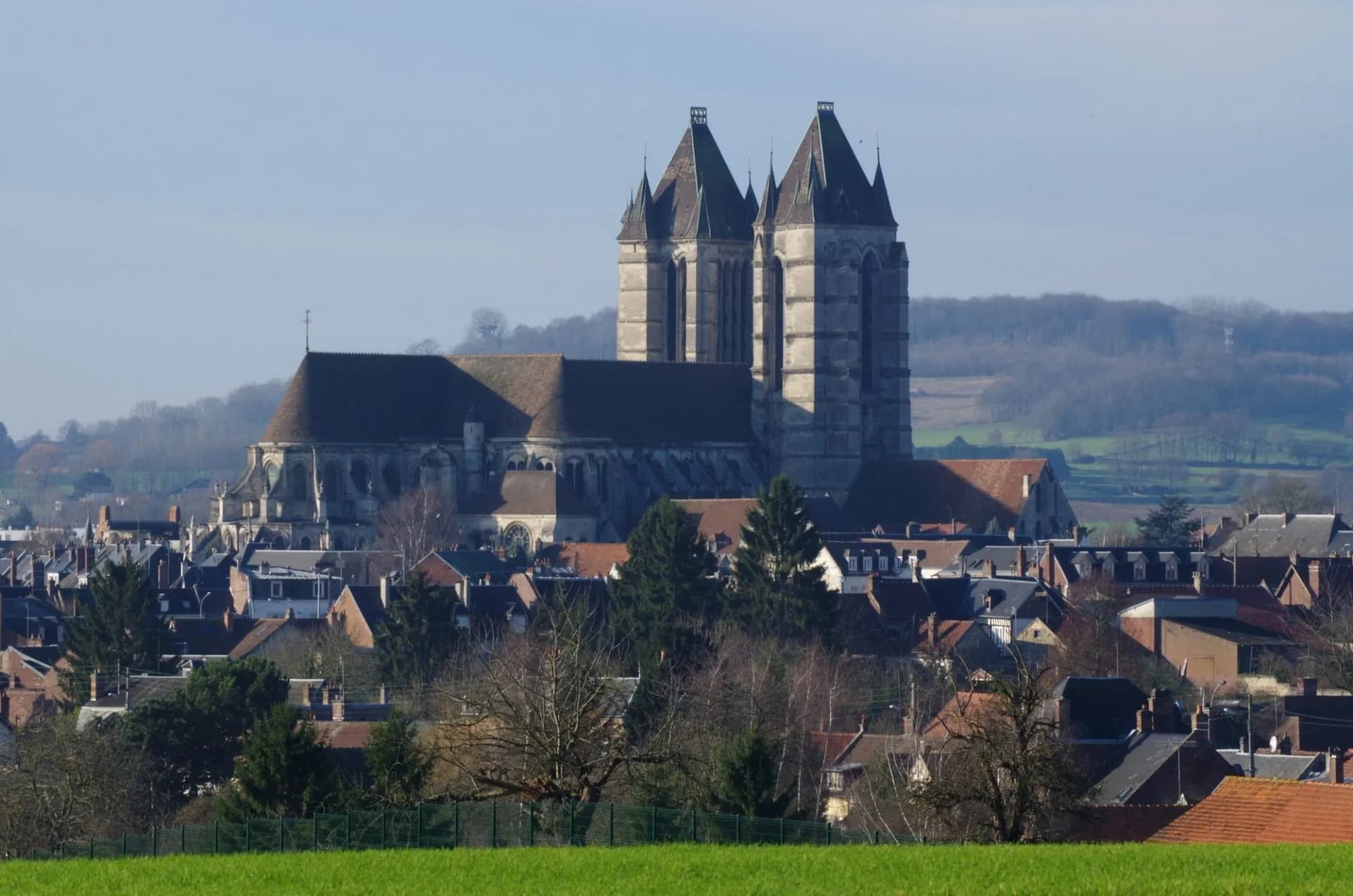 Large stone church towers over a town with red-roofed houses, backed by rolling hills.
