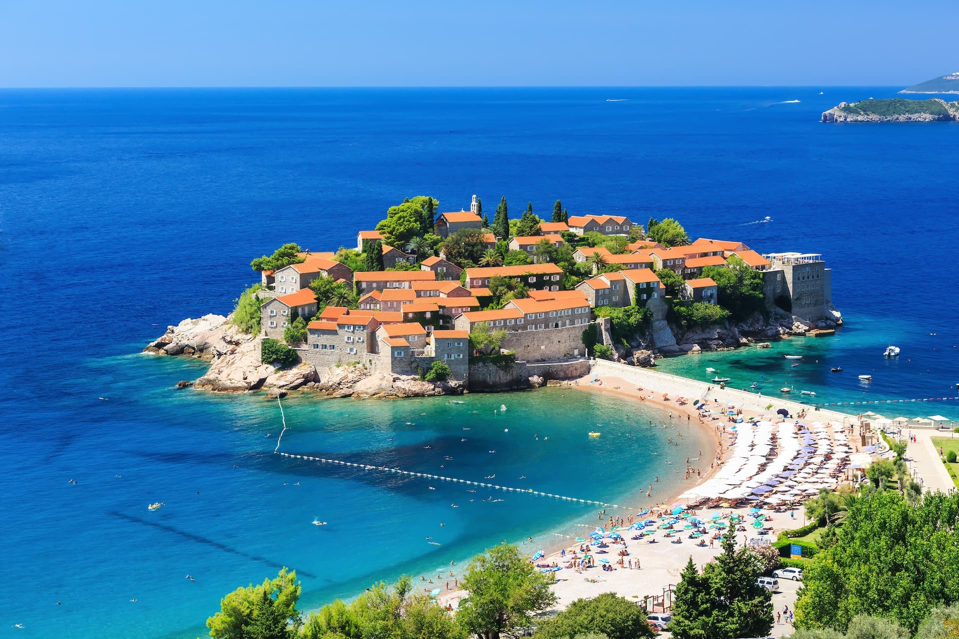 Sveti Stefan island resort with orange roofs connected to a busy beach on the Adriatic Sea in Budva, Montenegro.