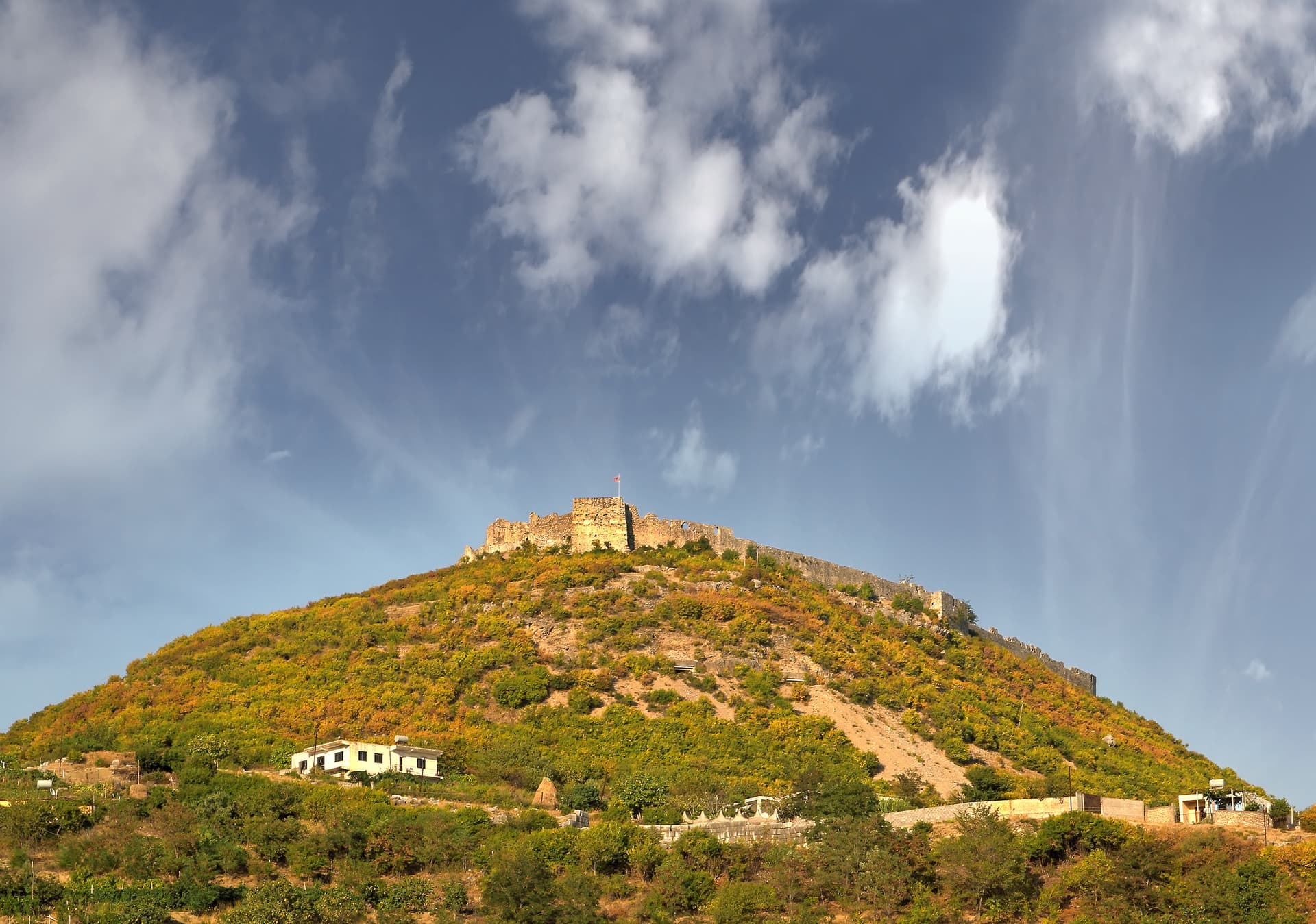 Lezha Castle ruins atop a scrub-covered hill under a blue sky with scattered clouds in Albania.