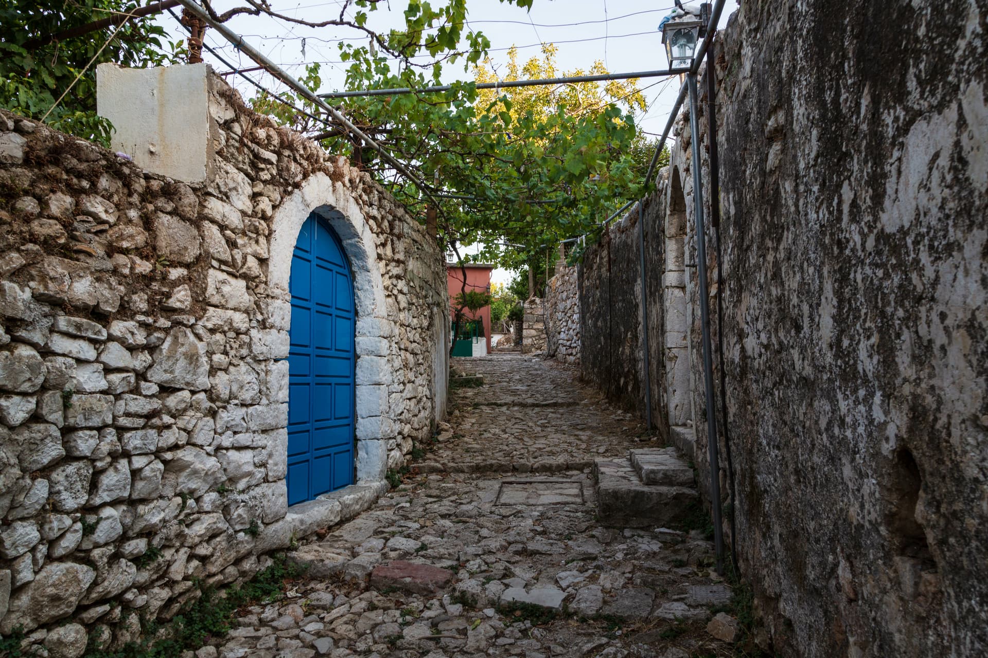 Cobblestone alley in Himare old town, Albania, with stone walls and a bright blue arched doorway.