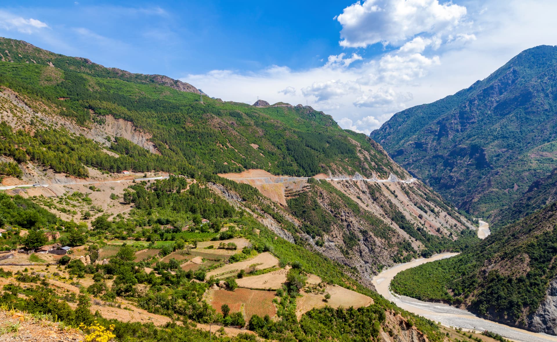 Mountain landscape in Albania with steep green slopes, a winding road, and a river in the valley.