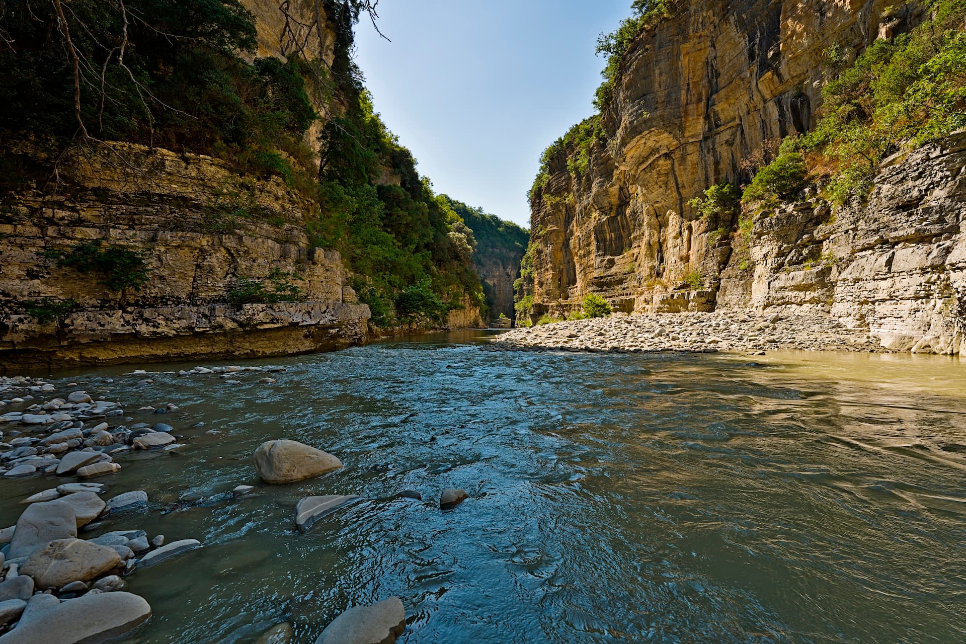 River flowing through Osum Canyon with steep, rocky cliffs and green vegetation in Albania.