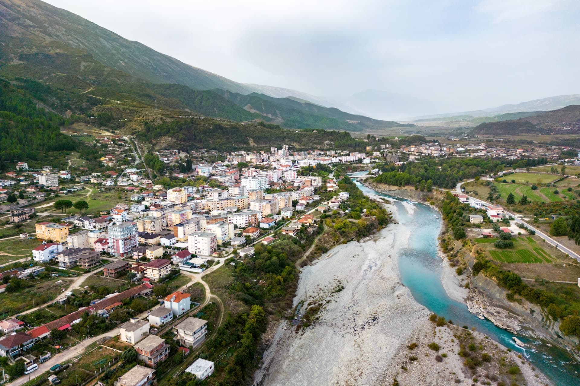 Aerial view of Përmet town nestled by the Vjosa River and green mountains in Albania.