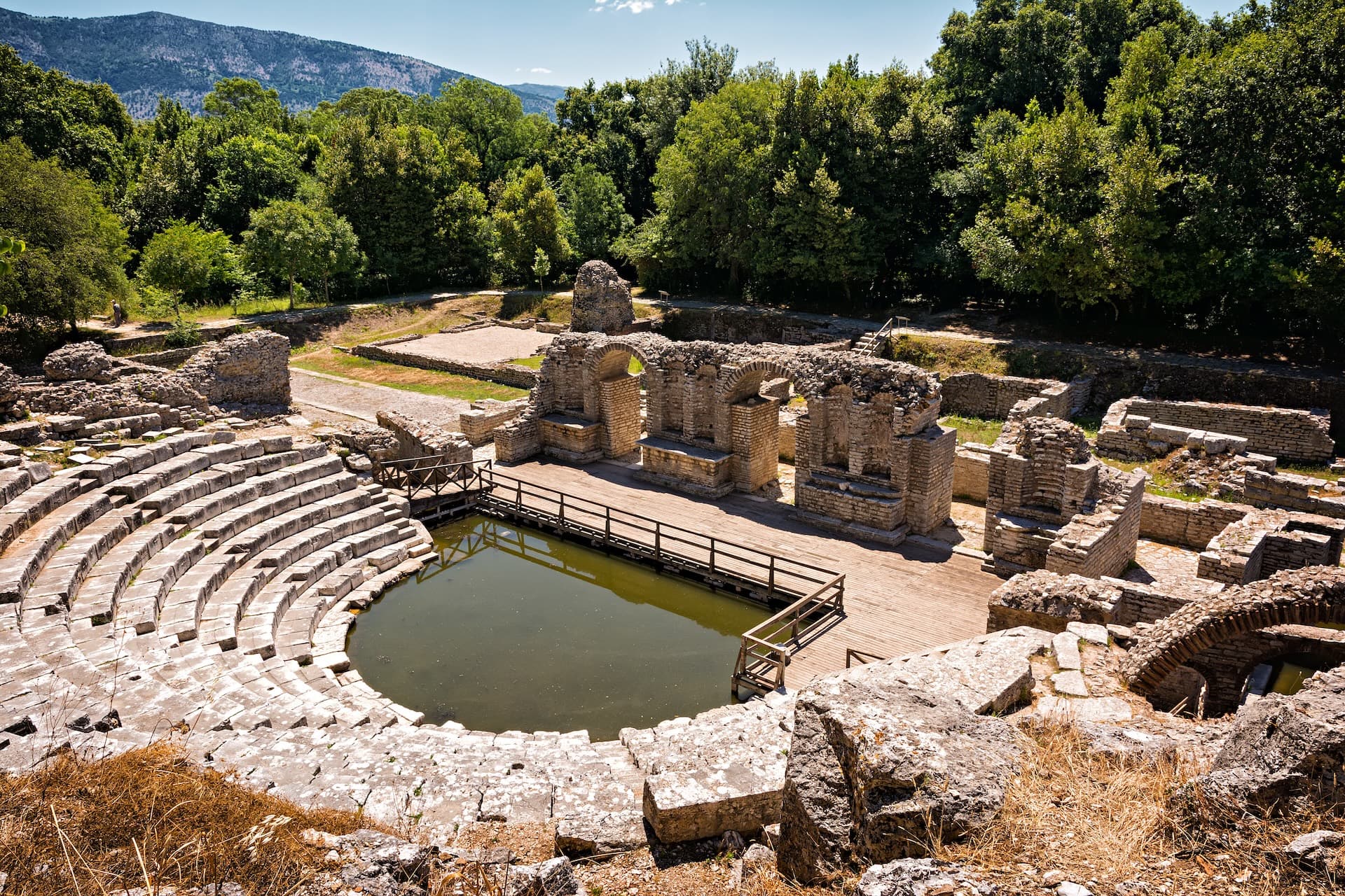Ancient theater ruins with stone seating and a central pool at Butrint National Park, Albania.