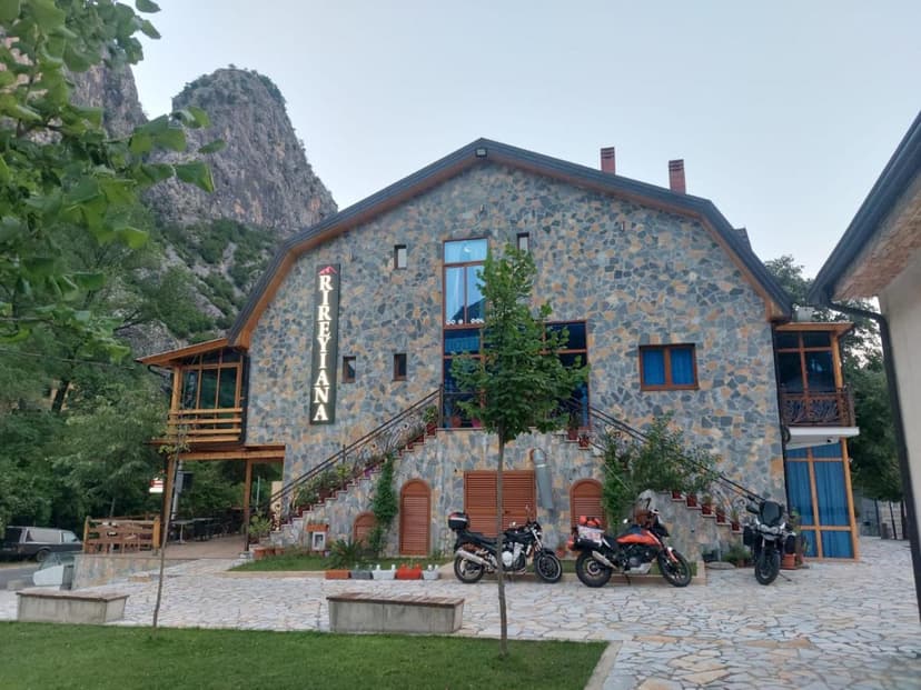 Stone building with Rireyana sign, motorcycles parked outside near mountains and trees