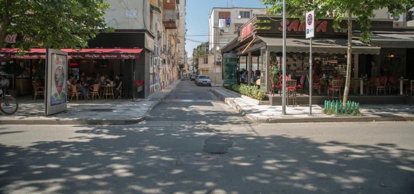 Street view of cafes with outdoor seating and apartment buildings in Tirana on a sunny day.