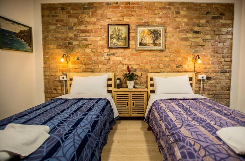 Twin beds with patterned blankets flanking a wooden nightstand against an exposed brick wall in Tirana room.
