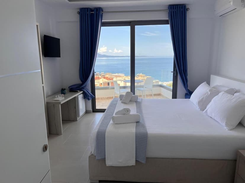 Hotel room with white bedding and blue curtains overlooking the sea view in Saranda