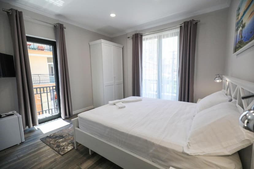 Hotel Peroni Korce guest room with white bedding, white wardrobe, and balcony access.