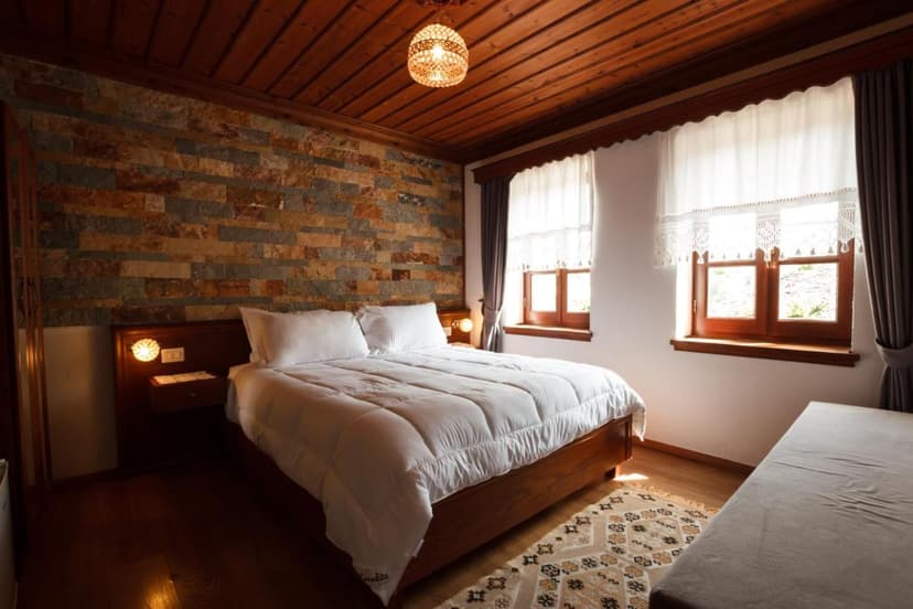 Hotel Pashai Gjirokaster room with wood ceiling, stone accent wall, and white bedding.