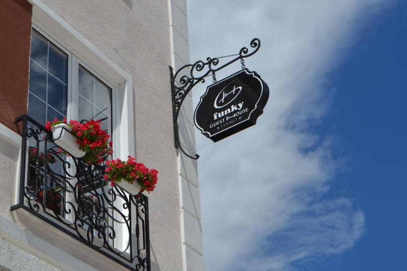 Funky Guest House sign hanging by window with red flowers on balcony against blue sky.