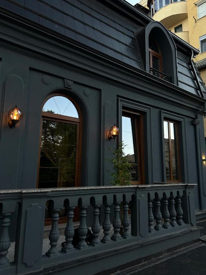 Dark gray building facade with arched windows, ornate balcony railing, and exterior lanterns at Fole Guest House Pogradec.