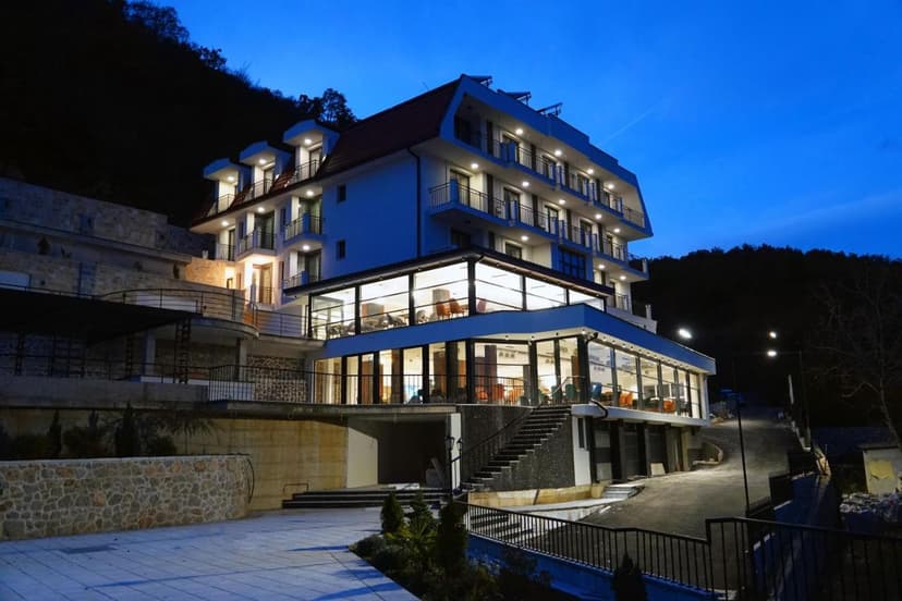 Dishli Hotel & Spa Struga exterior at dusk with illuminated glass restaurant and dark hillside background.