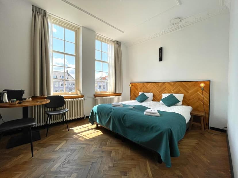 Bright hotel room with herringbone wood floor, teal bedding, and view of historic buildings in Zierikzee.