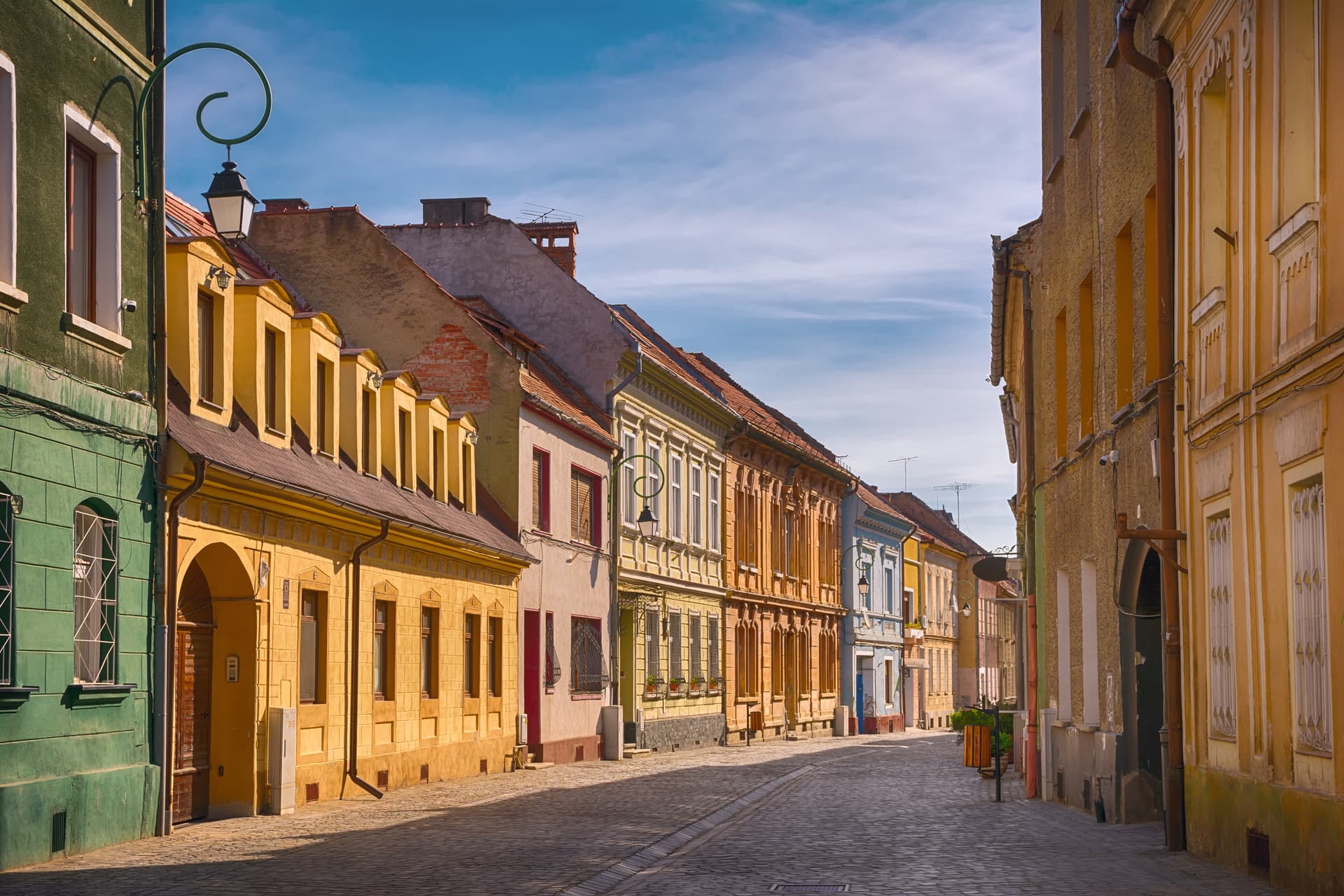 Cobblestone street lined with colorful historic buildings under a blue sky in Brasov, Romania.