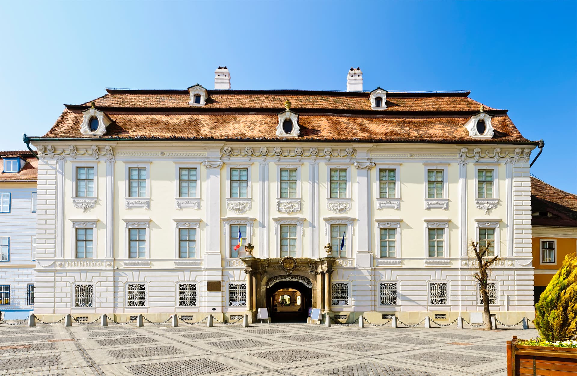 Brukenthal Palace in Sibiu with ornate facade, terracotta roof, and cobblestone square.