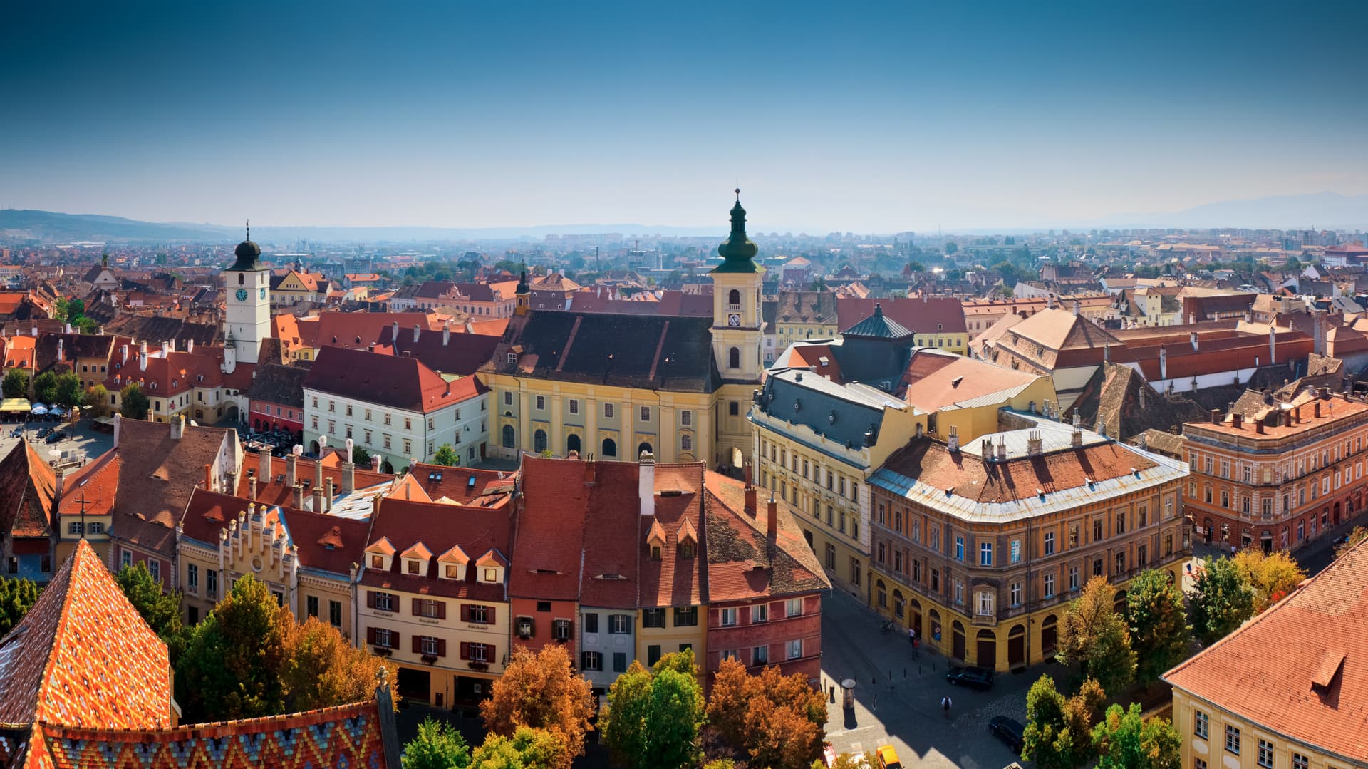 Panoramic view of Sibiu, Romania old town with red tile roofs and a prominent clock tower under a clear blue sky.