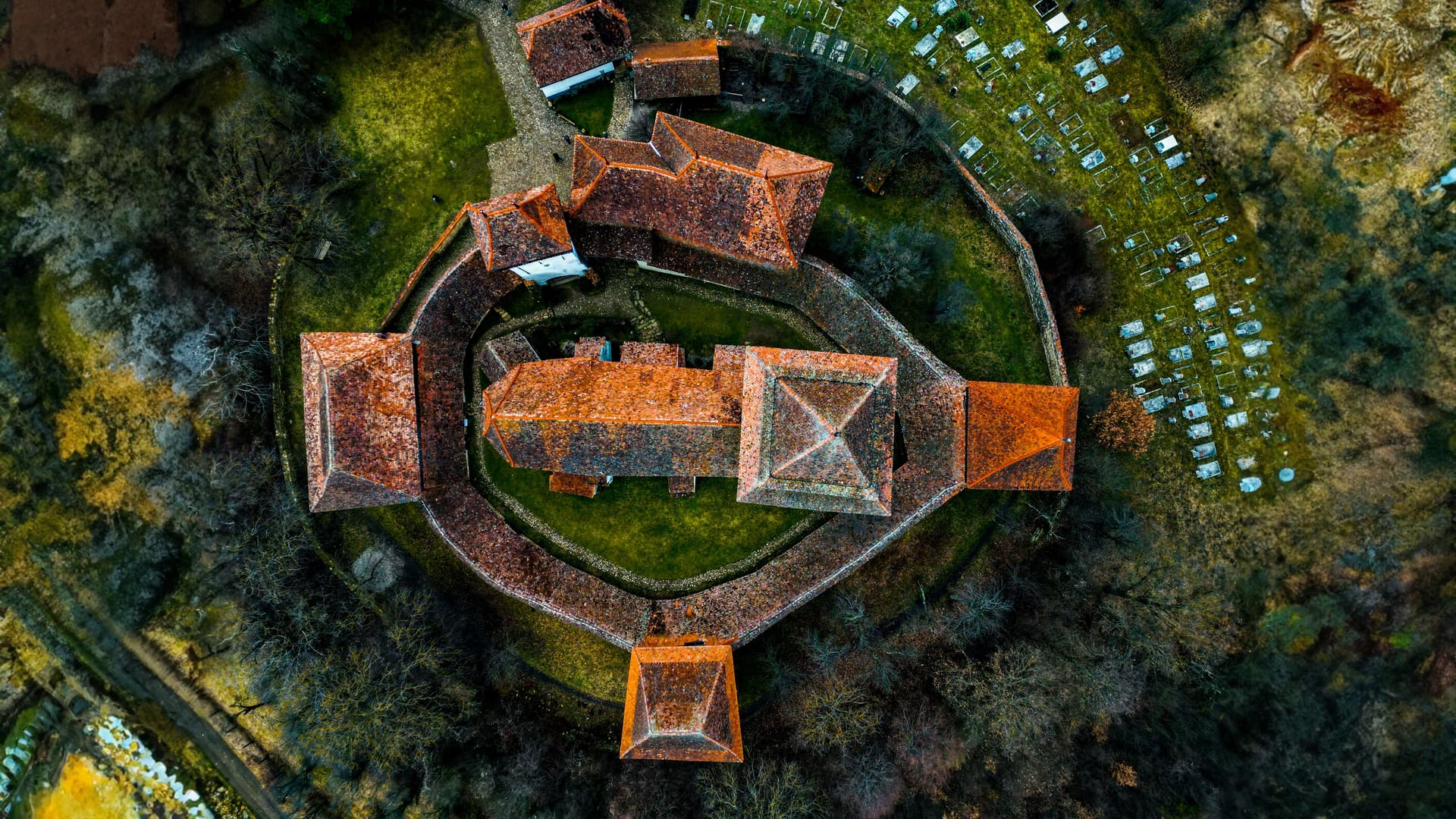 Aerial view of fortified church with orange tiled roofs and surrounding cemetery in Viscri, Romania.