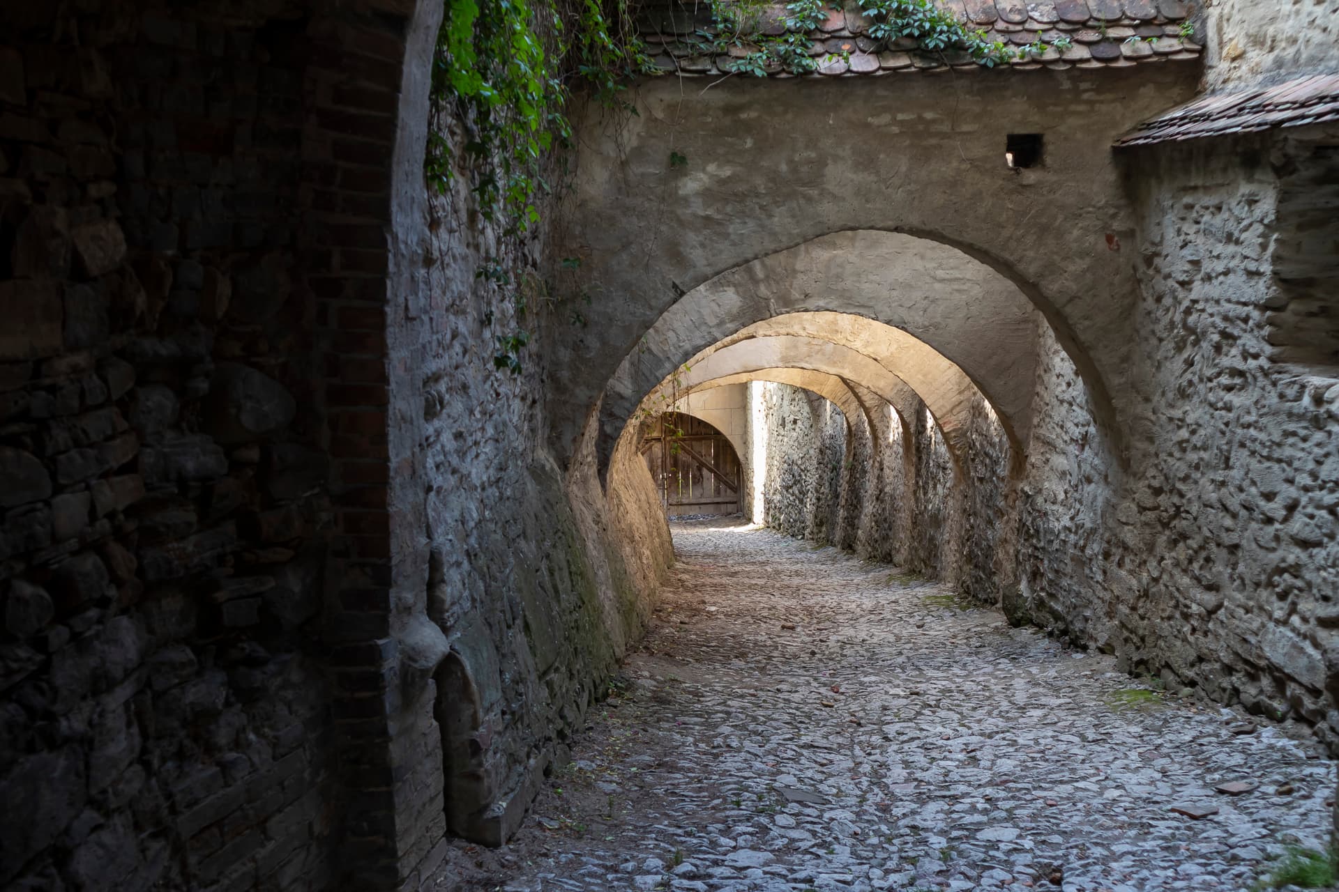 Cobblestone passageway under stone arches with ivy, Biertan Fortified Church, Romania.